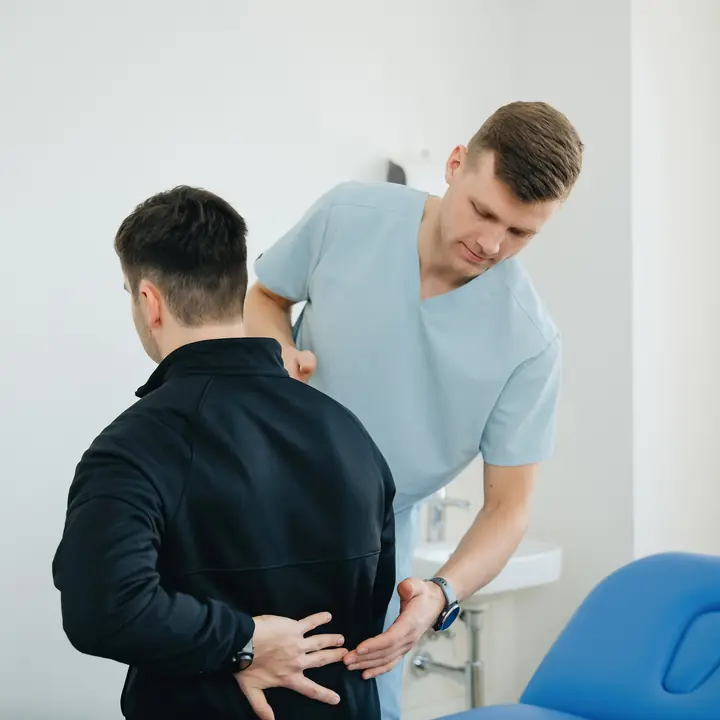 A patient holds his lower back while a physiotherapist checks how he bends.