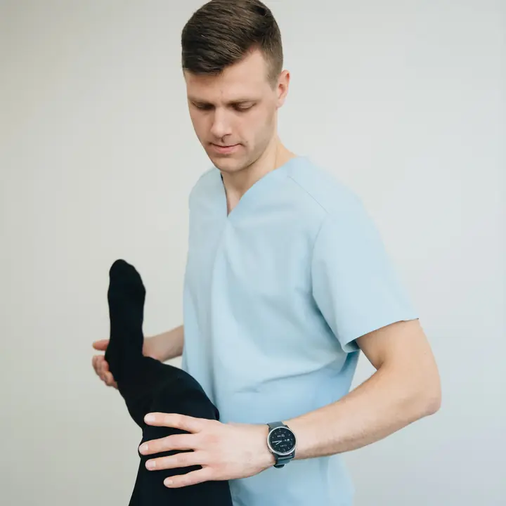 A physiotherapist holds a patient's raised leg at the knee and supports it with one hand.