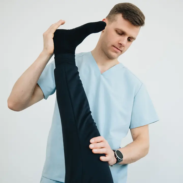 A physiotherapist lifts a patient's straight leg and supports it at the thigh during a rehabilitation exercise.