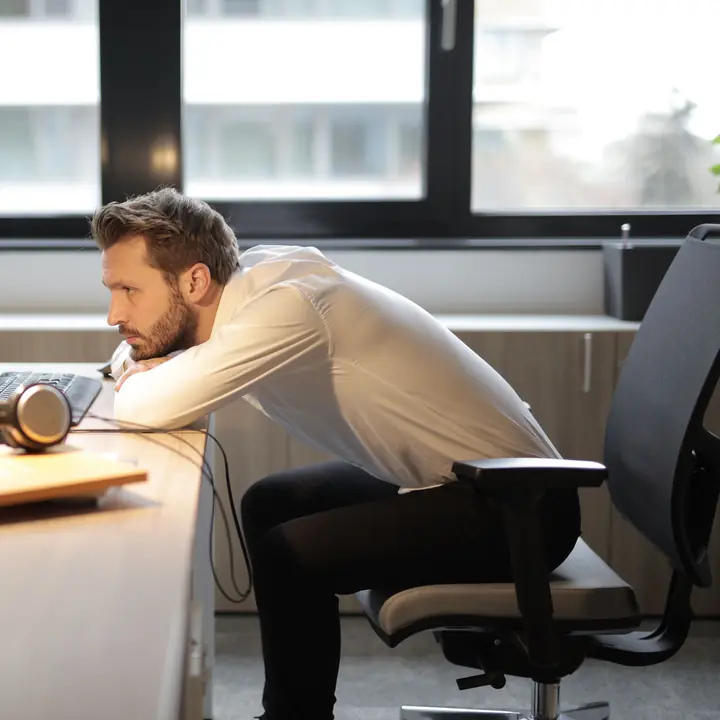 A man slumped forward over his desk, resting his head on his folded arms.